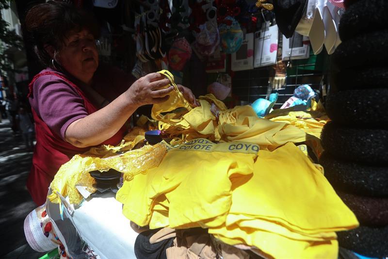 A woman with a purple and red shirt, curly hair, and earrings arranges men's and women's yellow underwear for sale.